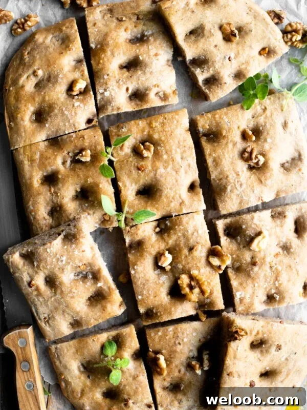 An overhead shot of a walnut focaccia cut into12 squares sprinkled with walnuts