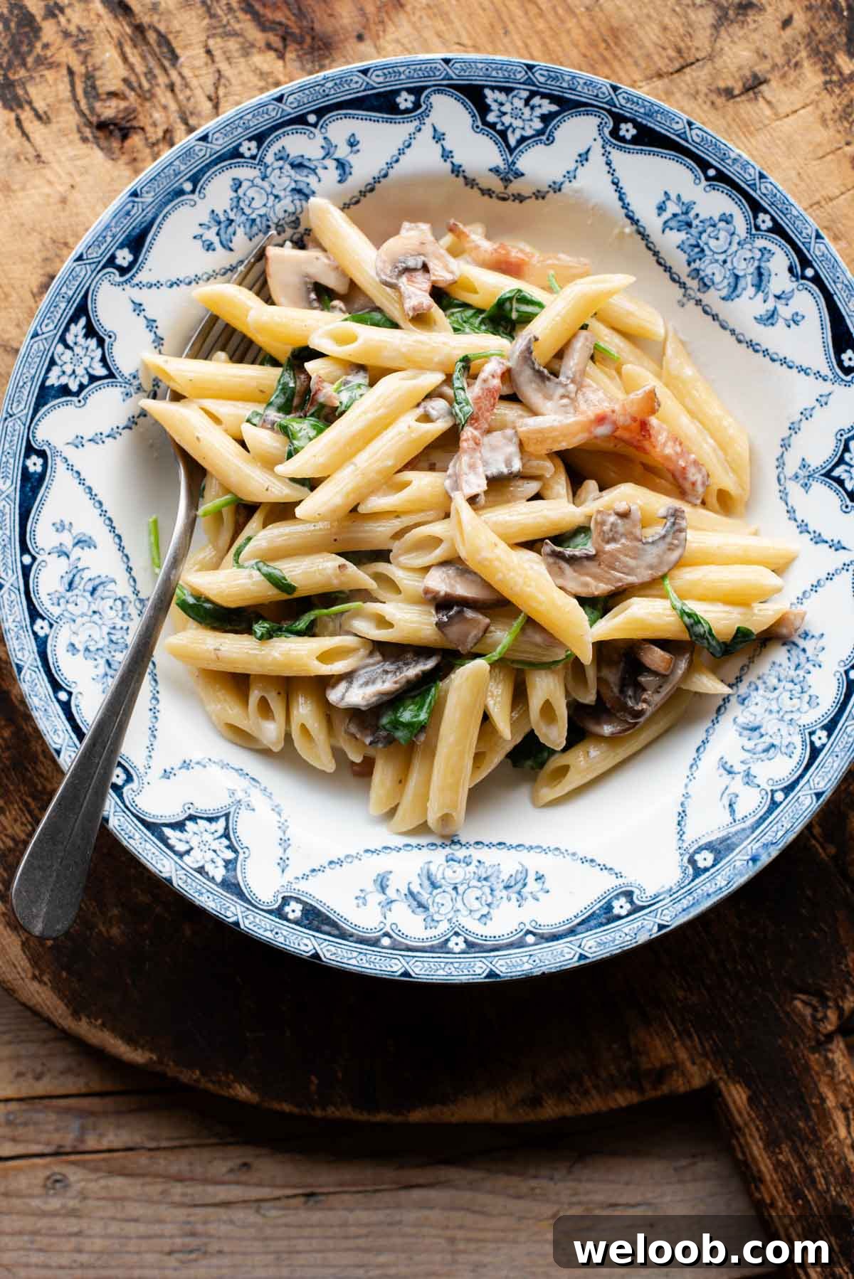 An overhead shot of mushroom spinach pasta in a blue and white bowl.