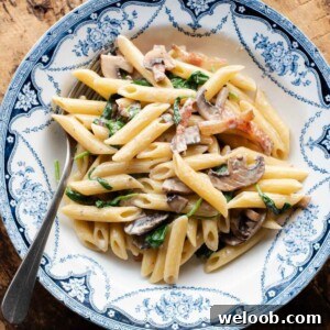 A cropped close up of mushroom spinach pasta in a blue and white bowl with a fork at the side.