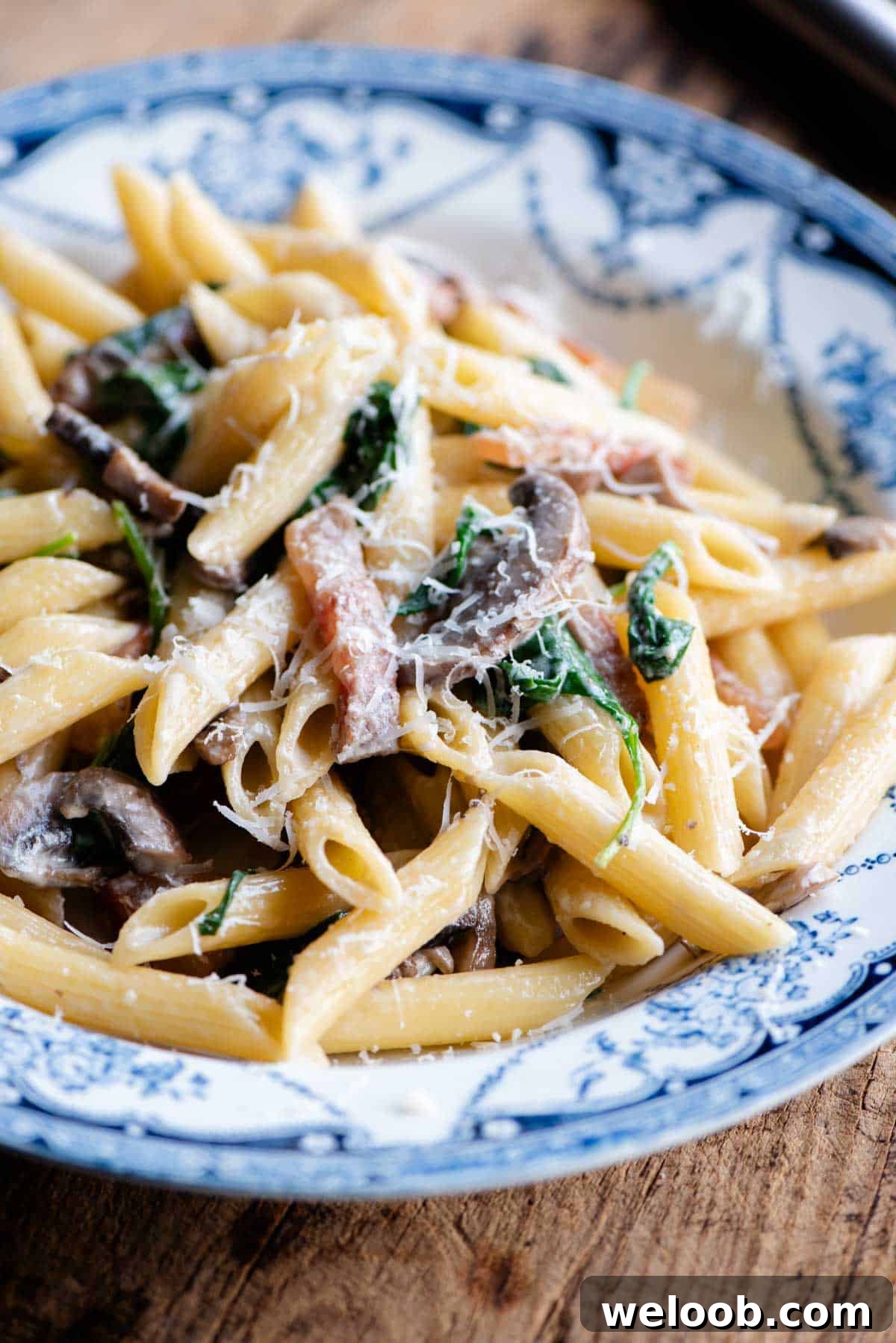 A close up of mushroom spinach pasta in a blue and white bowl.