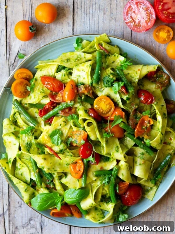An overhead shot of pasta with green beans, tomatoes and pesto
