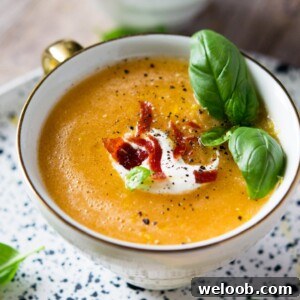 A close up of melon gazpacho in a mug topped with creme fraiche, crispy bacon and basil