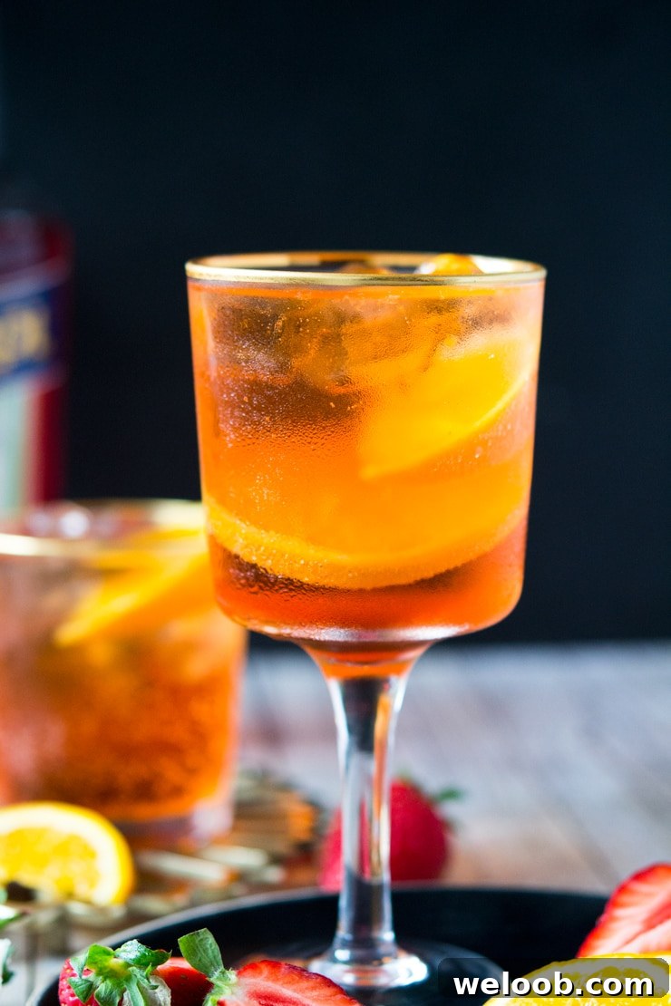 A close up of an Aperol spritz cocktail in a glass with strawberries and slices of orange at the side