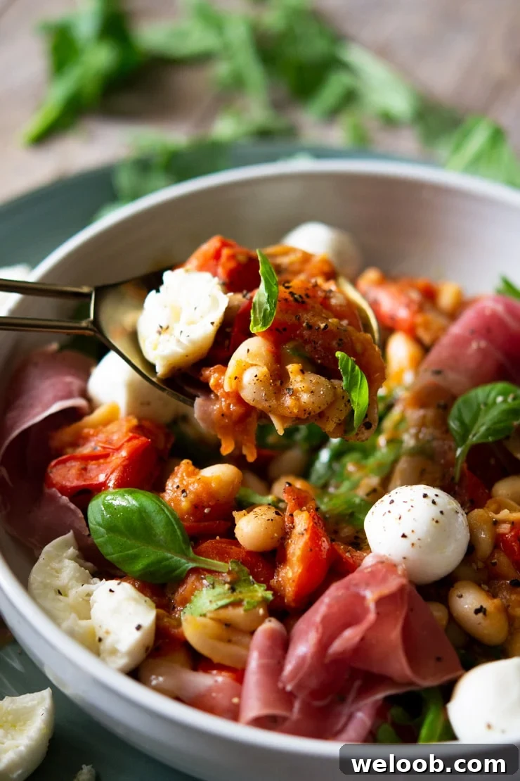 A close up of a white bean salad with tomato on a serving spoon