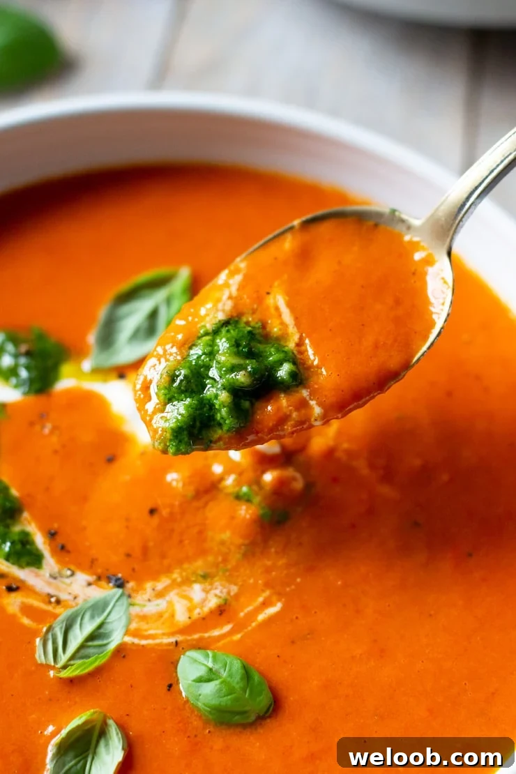 A spoon scooping up some roasted red pepper soup topped with pesto