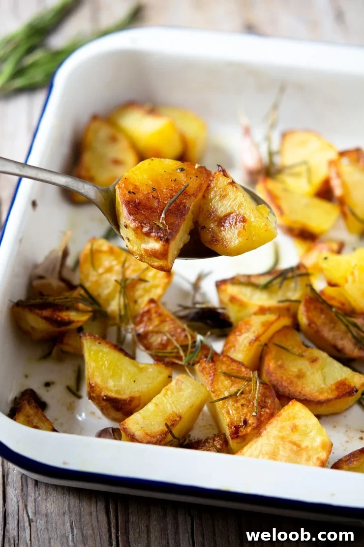 A spoon scooping up some Italian roast potatoes from a baking tray