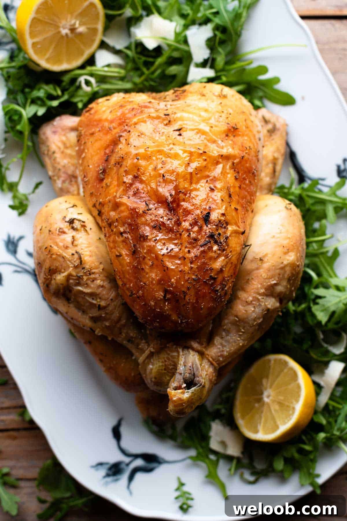 An overhead shot of a lemon roast chicken on a serving plate with arugula and lemon slices at the side.