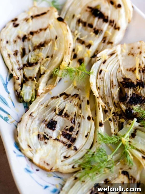 Slices of grilled fennel on a serving plate with lemon zest on top