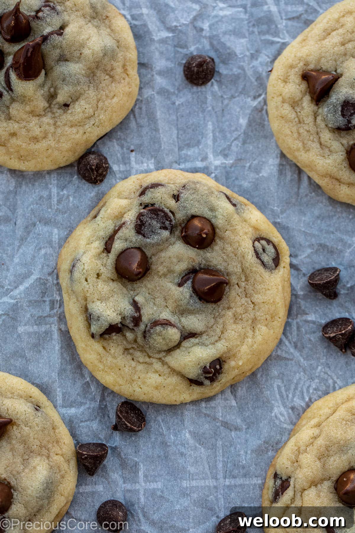 Chocolate chip cookies on parchment paper with chocolate sprinkles lying around.