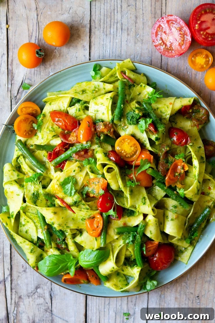 An overhead shot of pasta with green beans, tomatoes and pesto