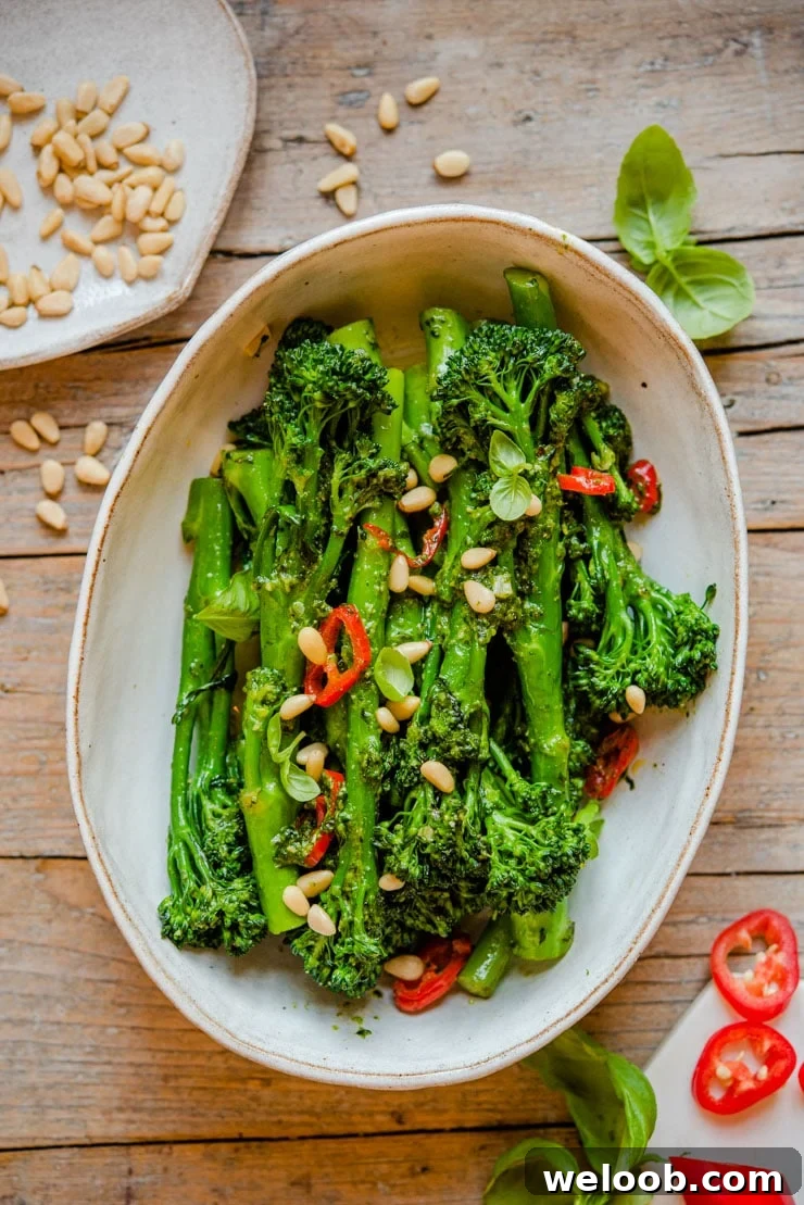 An overhead shot of sauteed broccolini in a serving bowl with pine nuts on top
