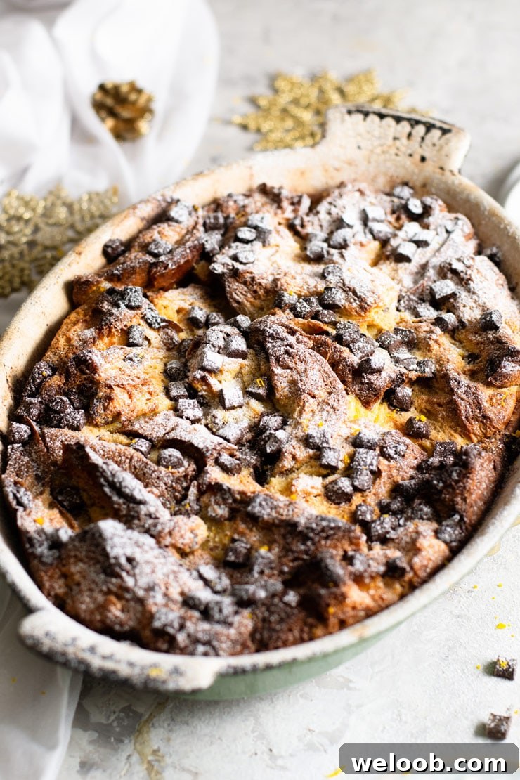 A close up of a panettone bread pudding in a rustic oval baking dish topped with chocolate chips and powdered sugar