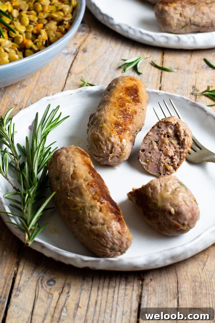 Two whole homemade sausages on a plate and another one cut in half with a rosemary sprig at the side