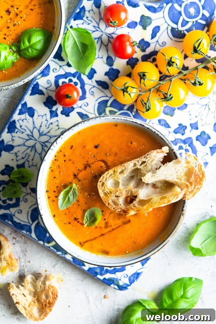 An overhead shot of roasted tomato soup in a bowl with basil and vine tomatoes at the side