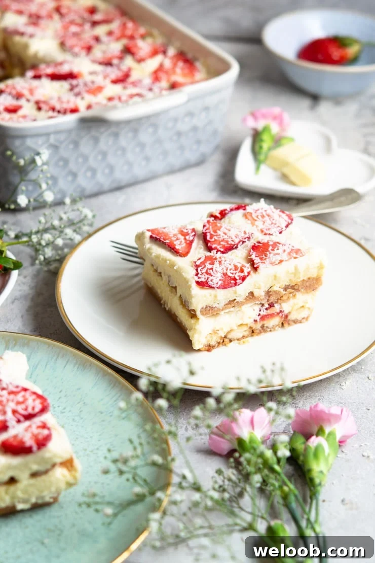 A slice of strawberry tiramisu on a white plate with flowers scattered around