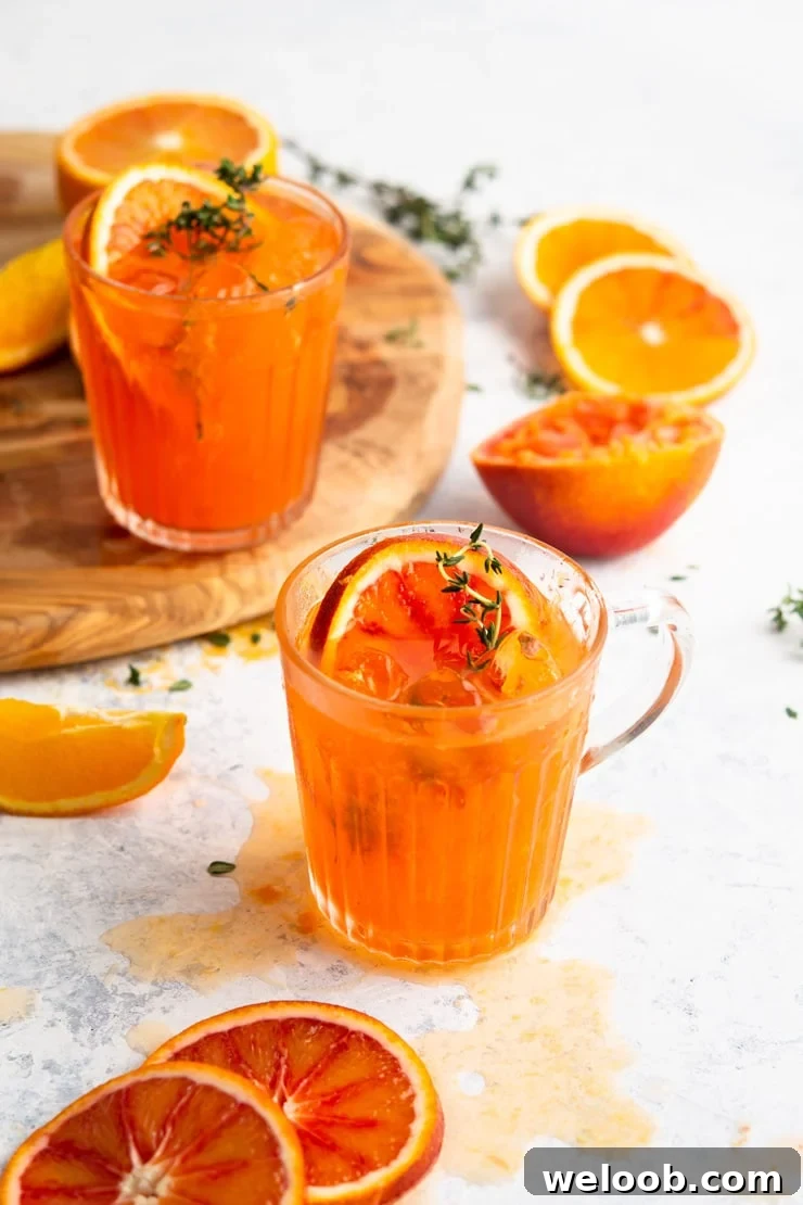 A blood orange cocktail in a glass with slices of orange all around and sprigs of thyme