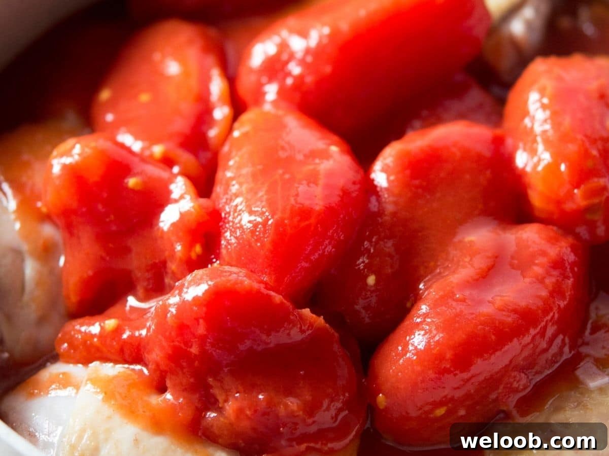 A close up of canned plum tomatoes in a pot with chicken.