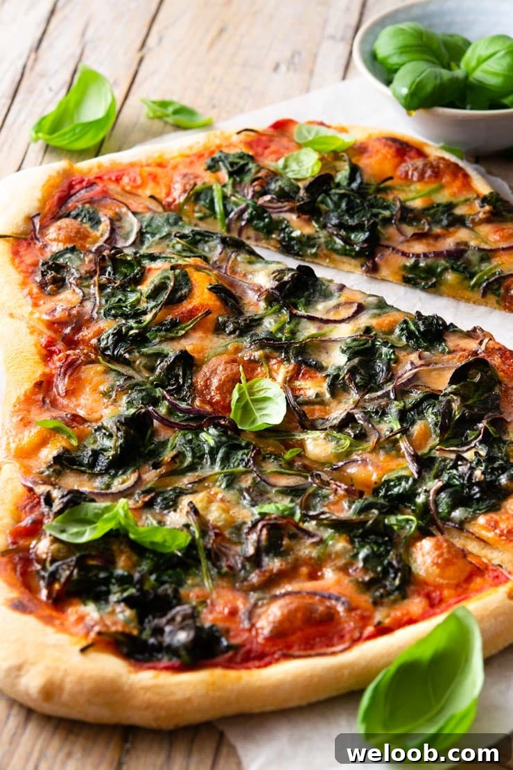 A close up of a spinach pizza cut into slices with gorgonzola cheese and red onion