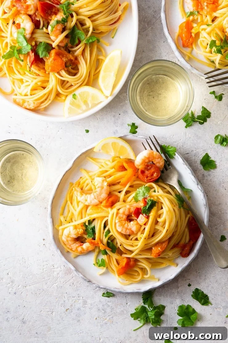 An overhead shot of shrimp linguine on a plate with glasses of white wine, parsley and lemon