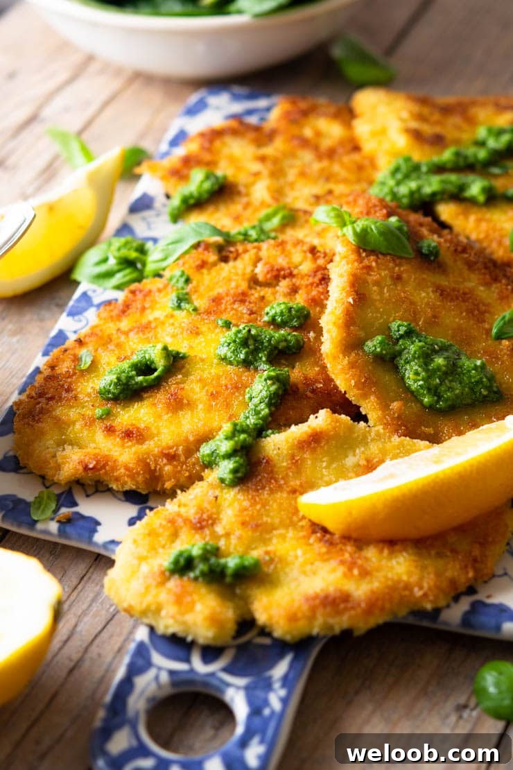 A side shot of breaded chicken cutlets on a blue serving board drizzled with pesto and lemon juice