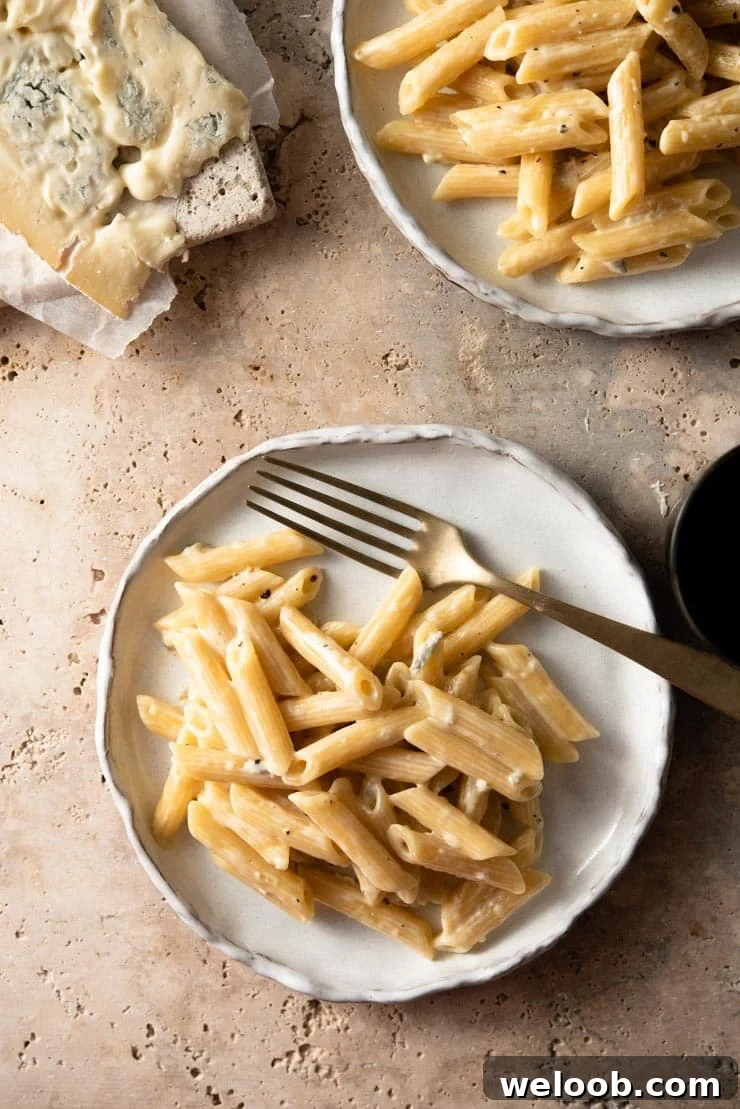 An overhead shot of plates of pasta with gorgonzola sauce and a block of melting gorgonzola in the background
