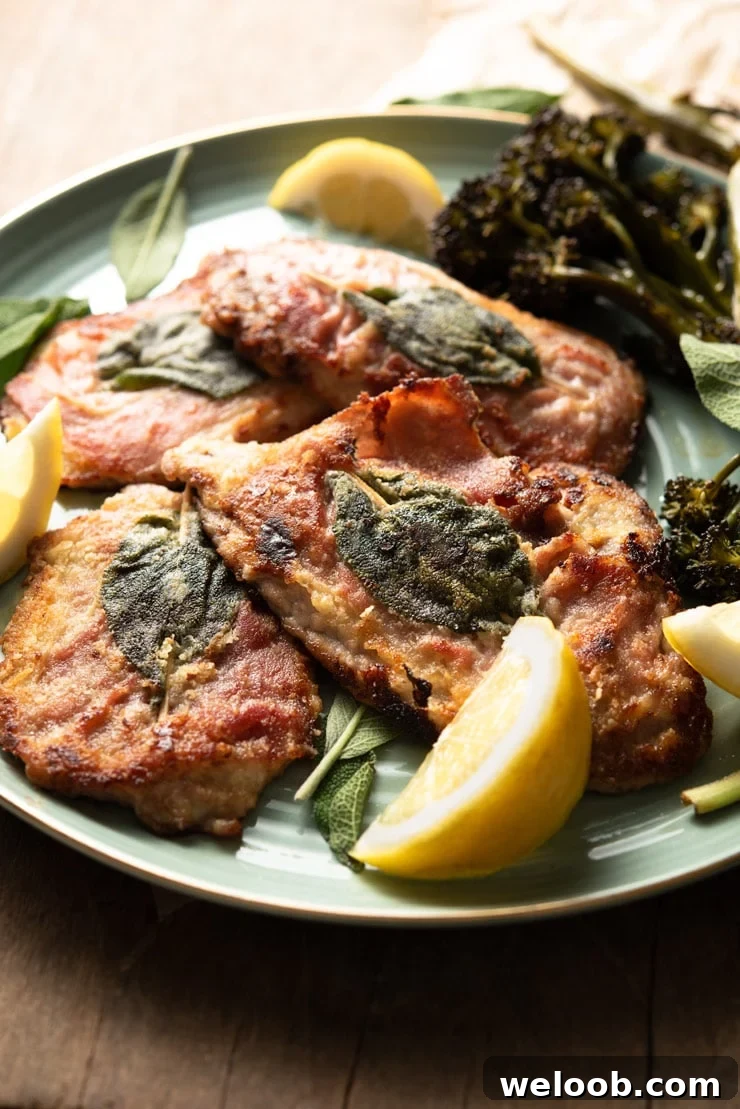 A side shot of veal saltimbocca with prosciutto and sage on a plate with lemon wedges
