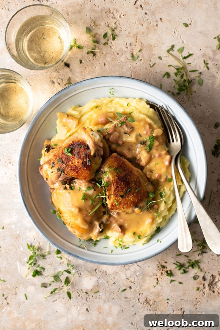 An overhead shot of creamy Tuscan chicken in a blue bowl with mashed potatoes and glasses of white wine