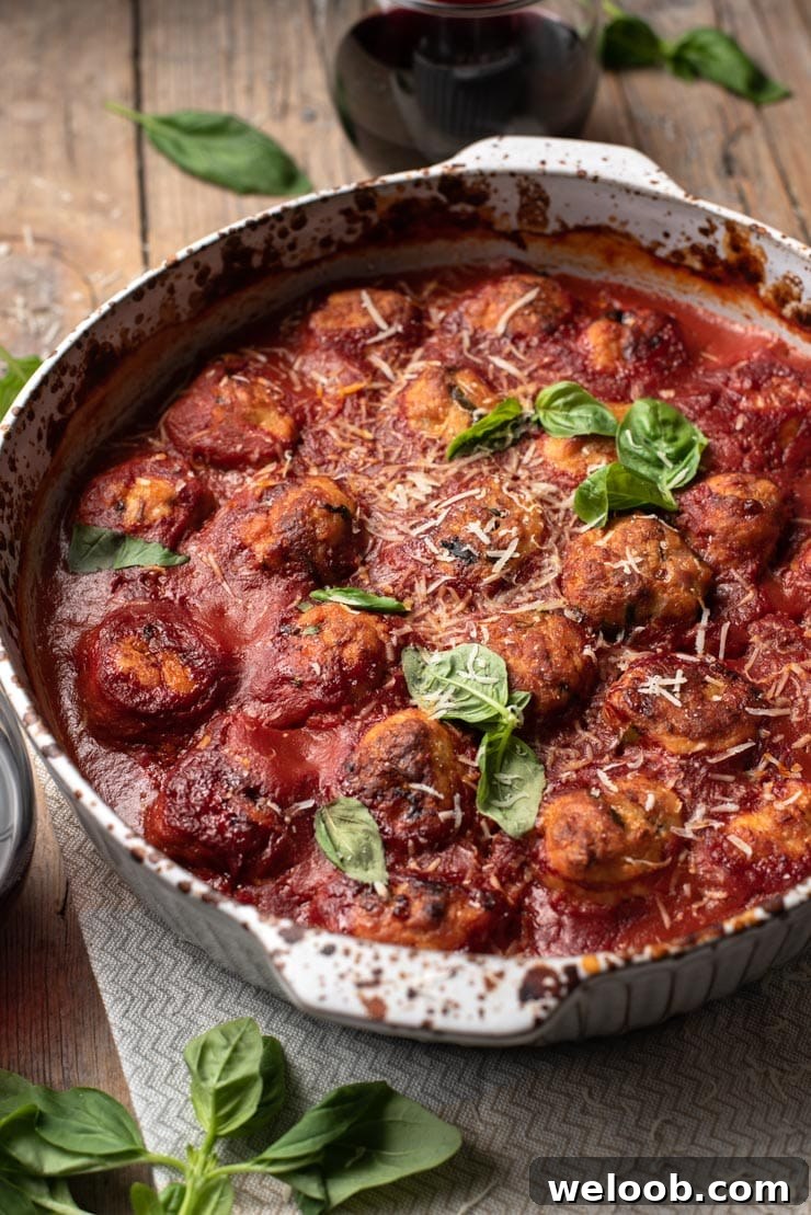 A close up of baked chicken meatballs in a baking dish with basil and parmesan on top