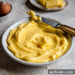A close up side shot of softened butter in a bowl with a knife at the side.