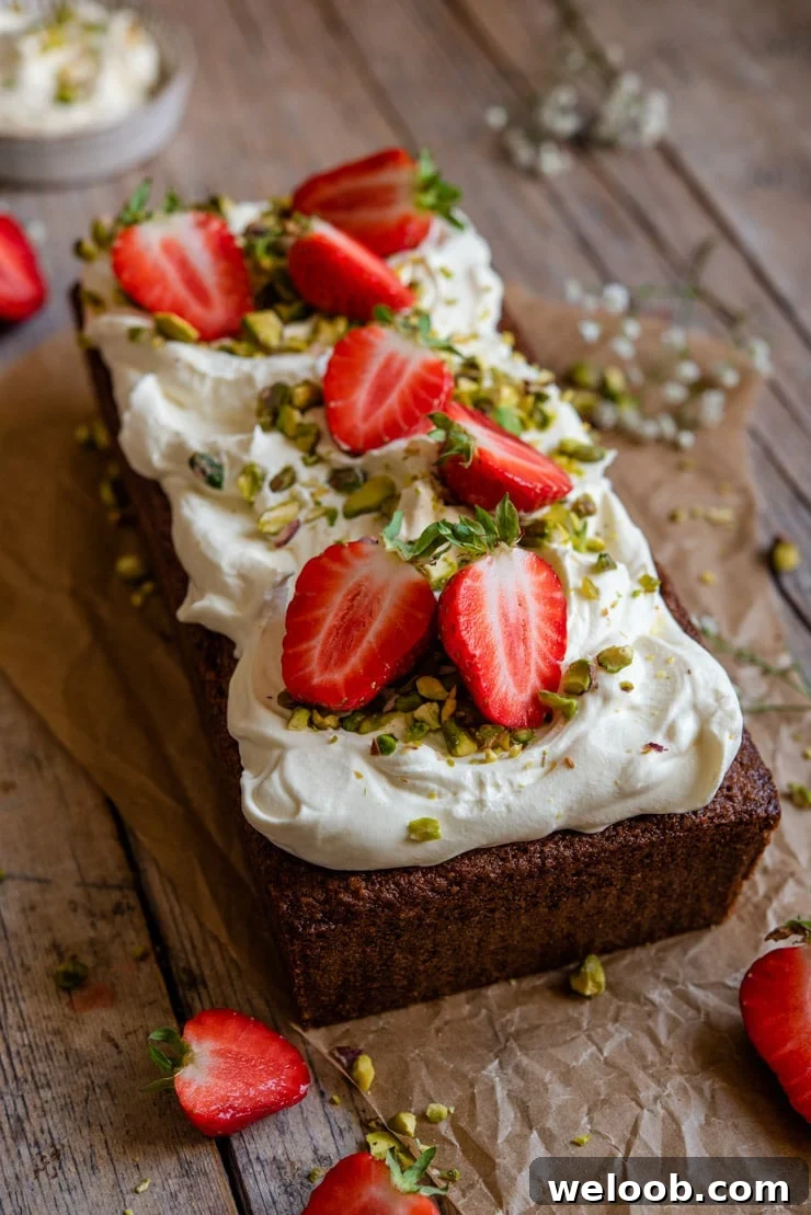 A side shot of a pistachio cake topped with whipped cream and strawberries