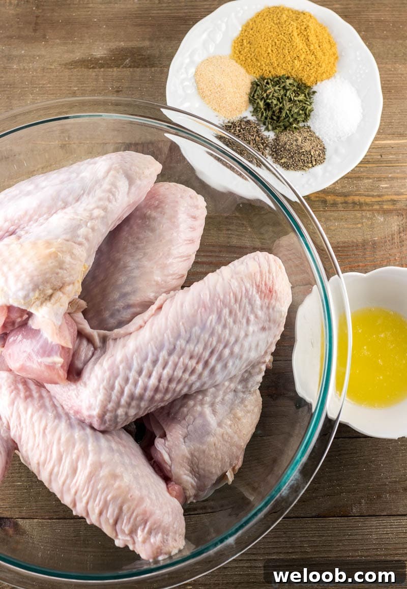 Fresh turkey wings in a bowl, spices and herbs on a plate, and melted butter in a small bowl.