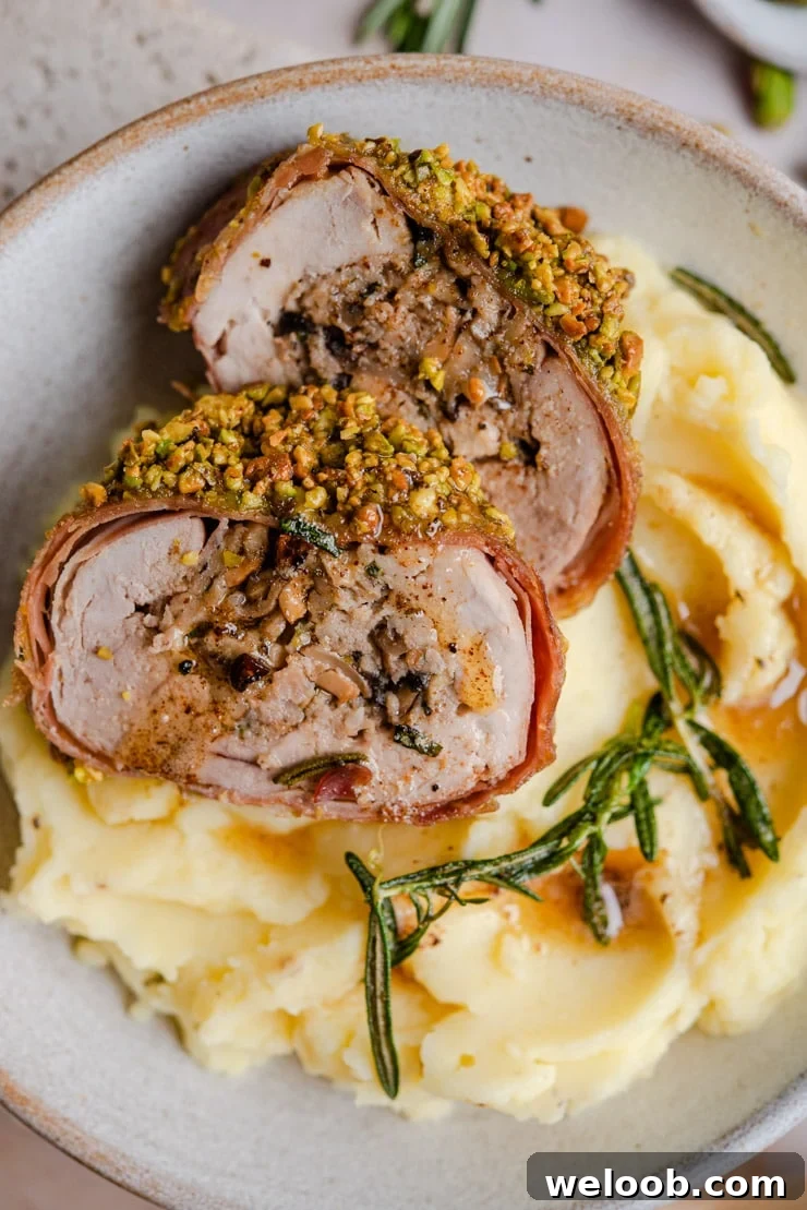 A close up of stuffed pork tenderloin sitting on top of mashed potatoes