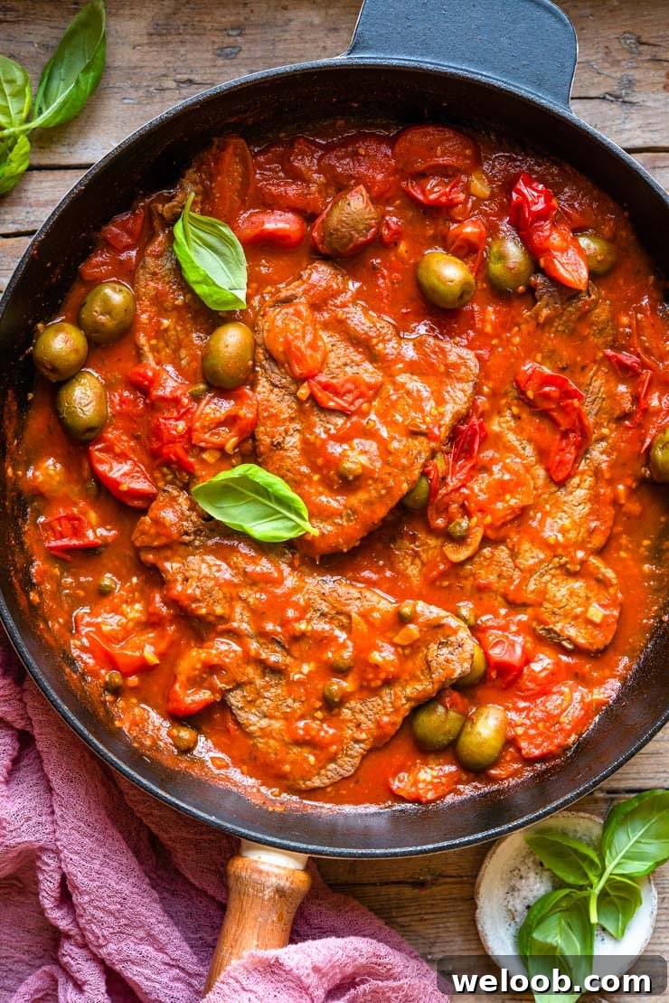 Steak Pizzaiola: steak in a tomato sauce with cherries, olives and basil Overhead shot of a skillet with steak in a tomato sauce with olives and basil