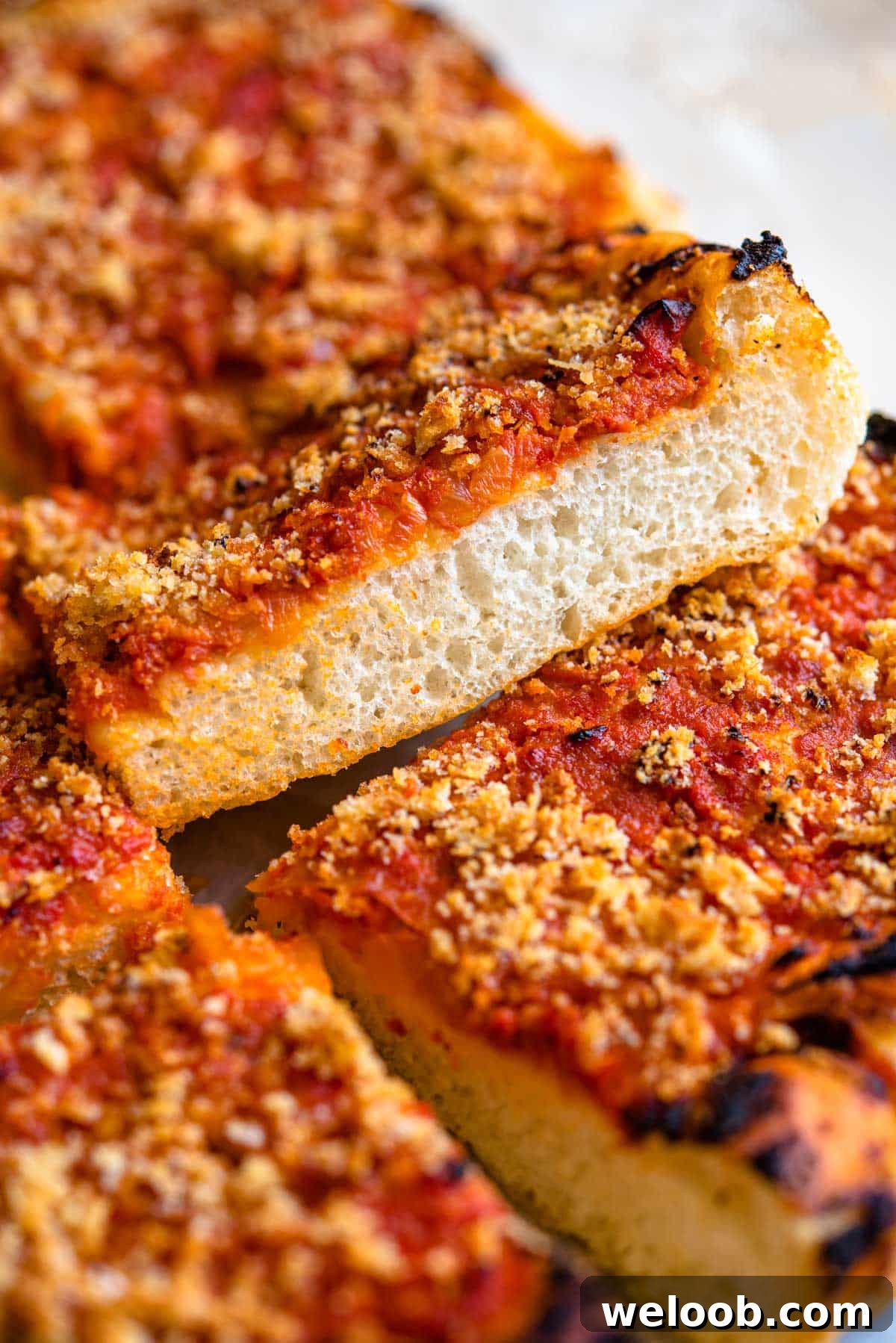 A side shot of a thick pizza crust that's light and airy topped with tomato sauce