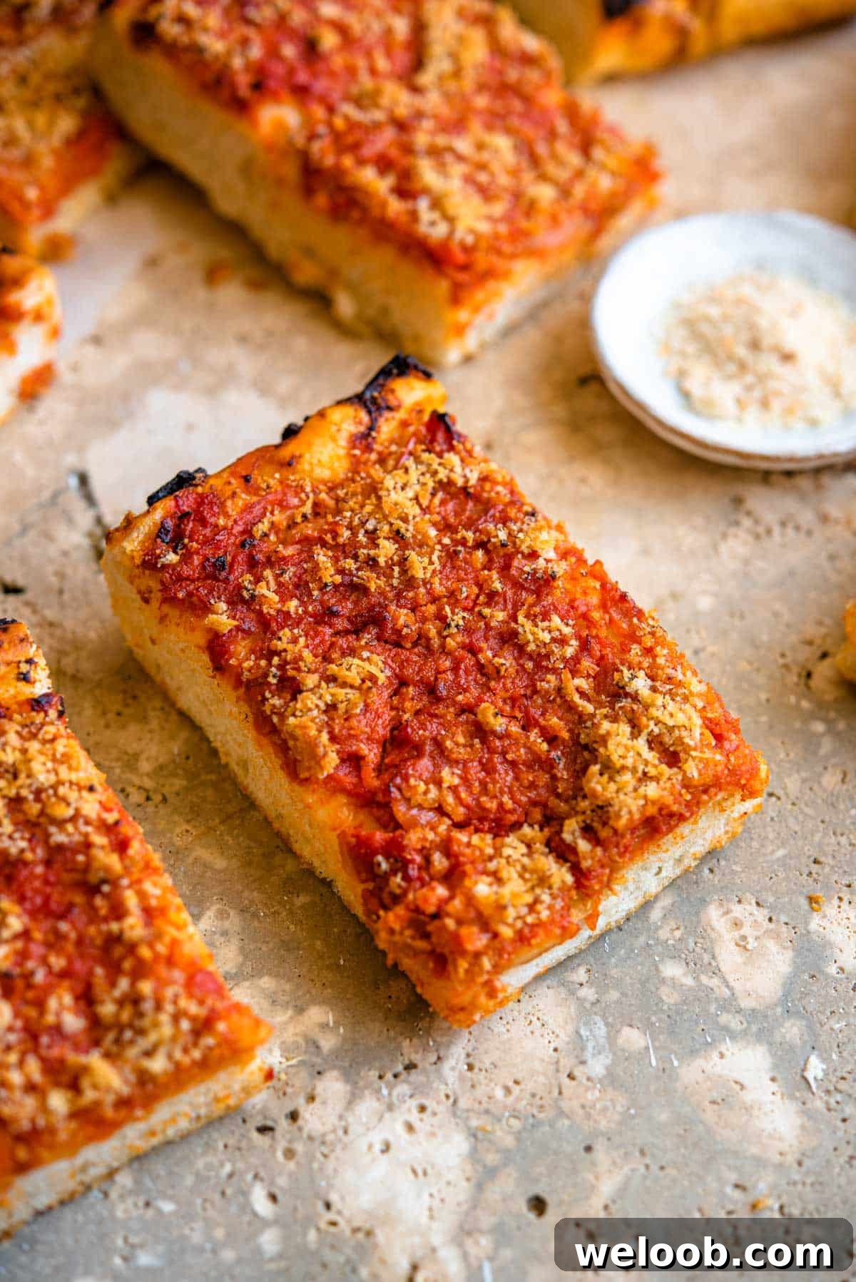 A close up of a slice of Sicilian pizza with breadcrumbs at the side