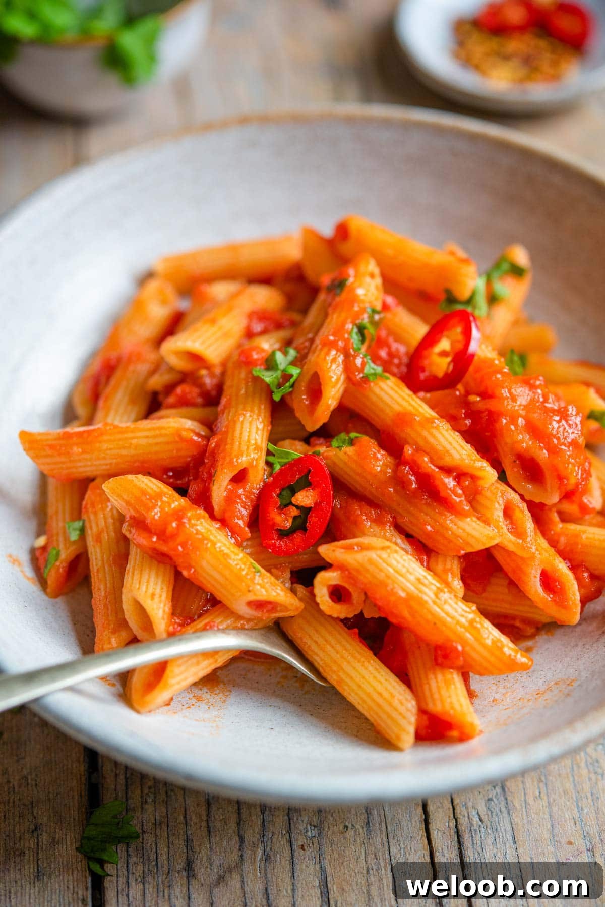 A close up of penne arrabbiata in a rustic bowl with a fork