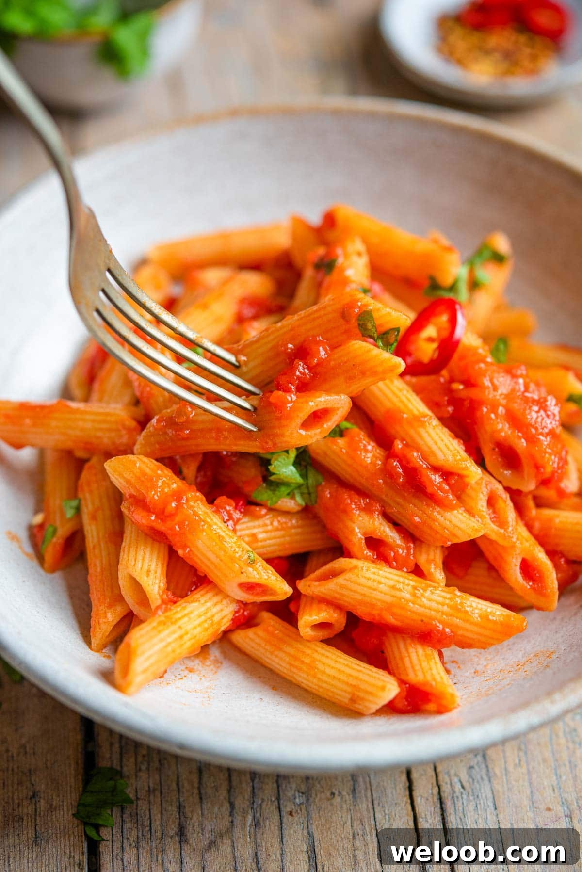 A close up of a fork picking up penne pasta from a bowl