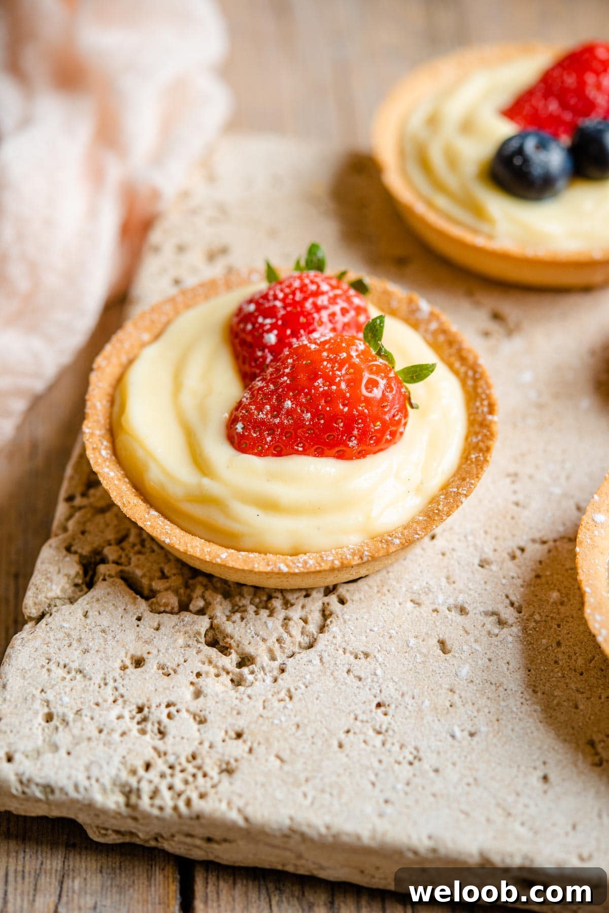 A small individual sized pie crust filled with Italian pastry cream and topped with two slices of strawberry.
