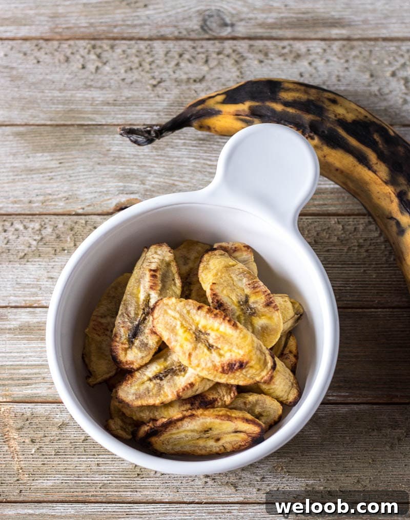 Baked Plantains in a bowl with one whole ripe plantain