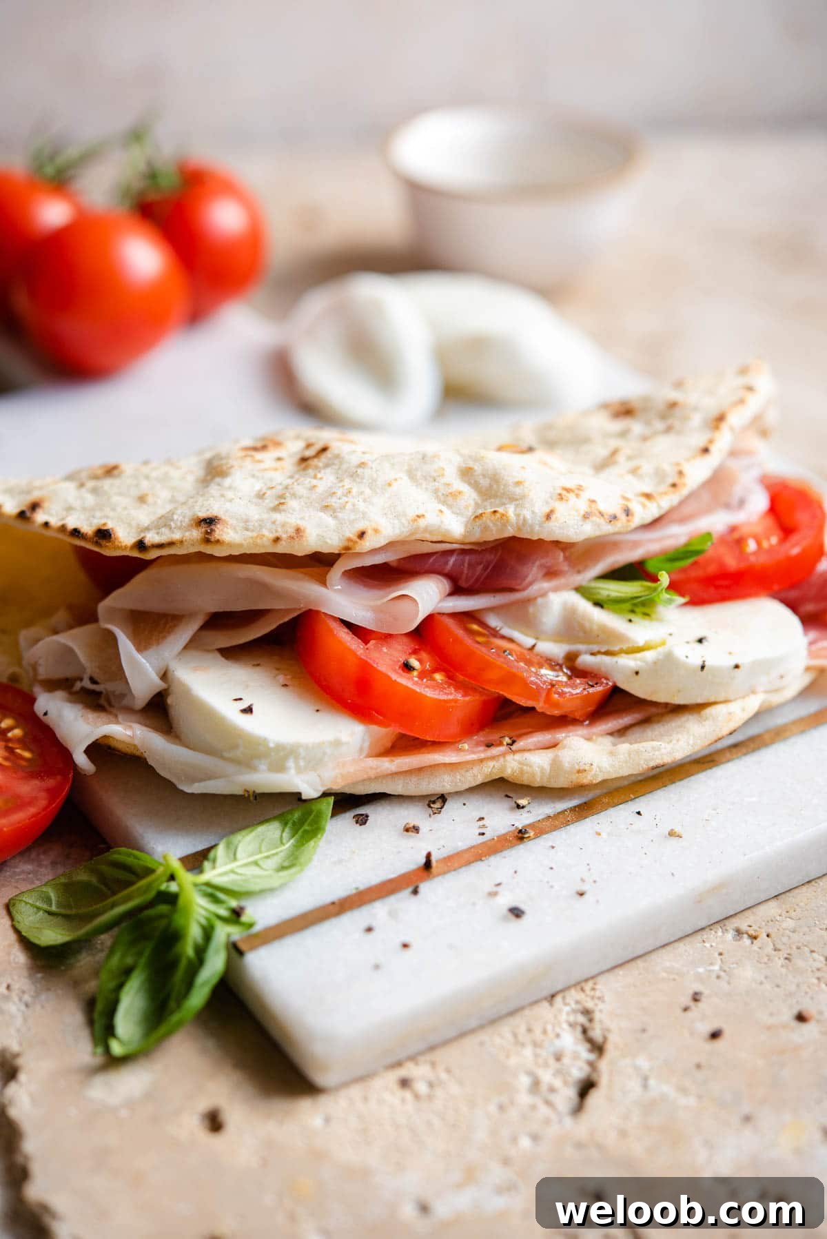 A Piadina flatbread stuffed with tomatoes, mozzarella and prosciutto sitting on a marble board