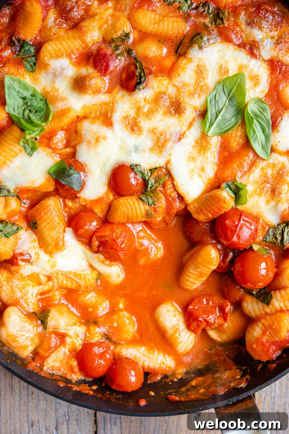 A close up of gnocchi in a skillet with a tomato sauce, mozzarella and basil