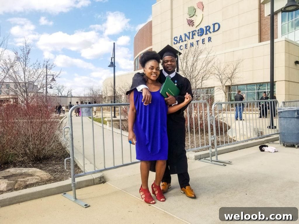 Man in graduation gear with a woman in a blue dress in front of the Sanford Center.