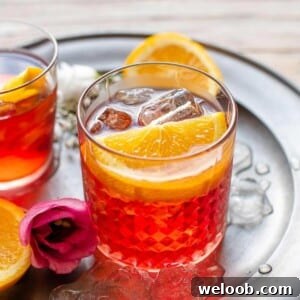 A close up of a Negroni cocktail on a pewter plate garnished with orange slices and a rose sitting beside it