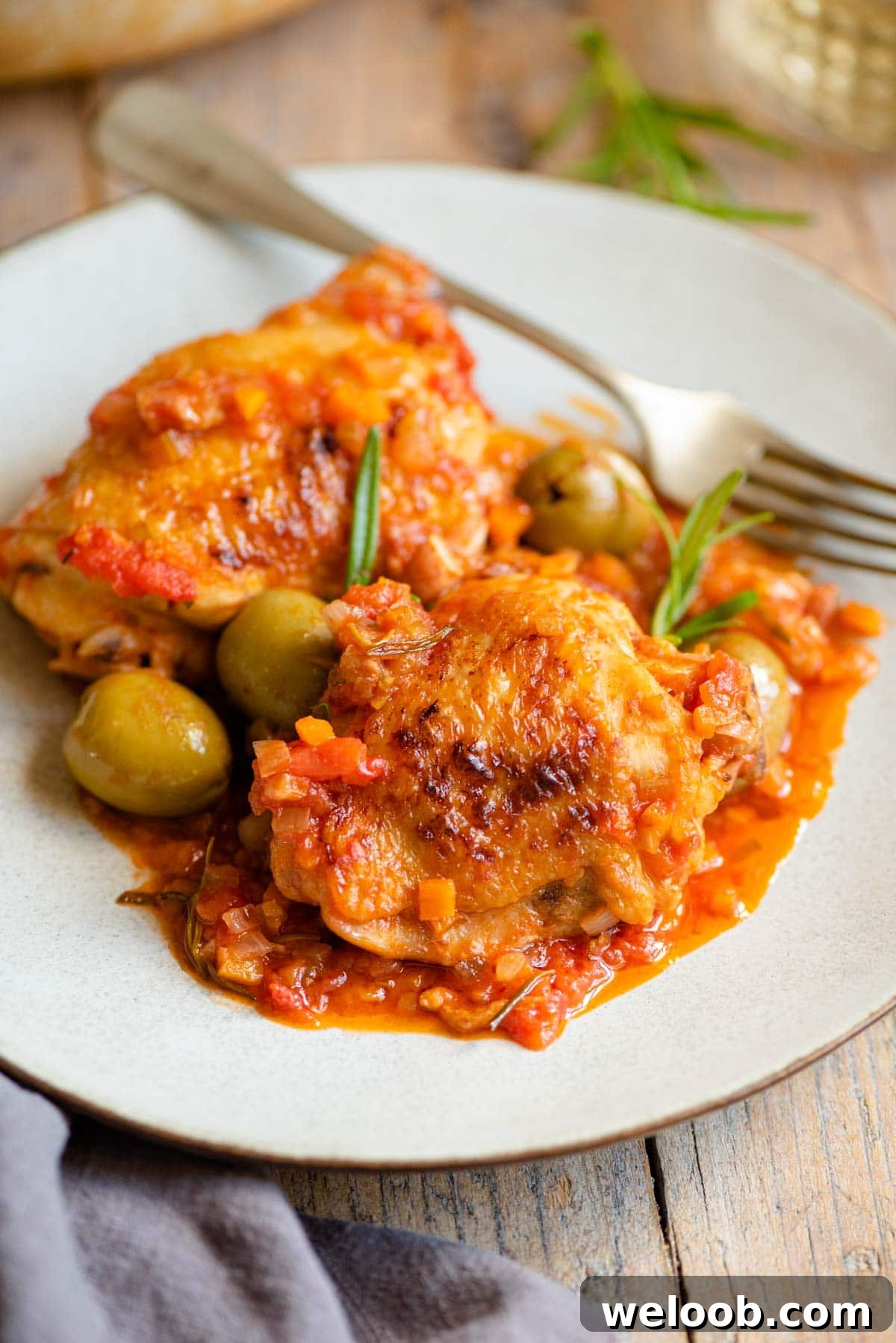 Two chicken thighs on a plate with a tomato and vegetable sauce and olives