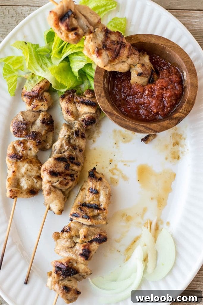 Chicken skewers with a wooden bowl of hot sauce and some vegetables