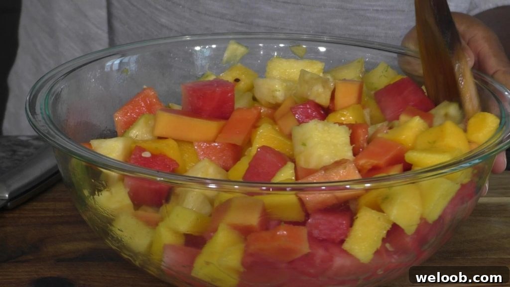 fruit salad in a large mixing bowl, hand mixing salad with a wooden spoon