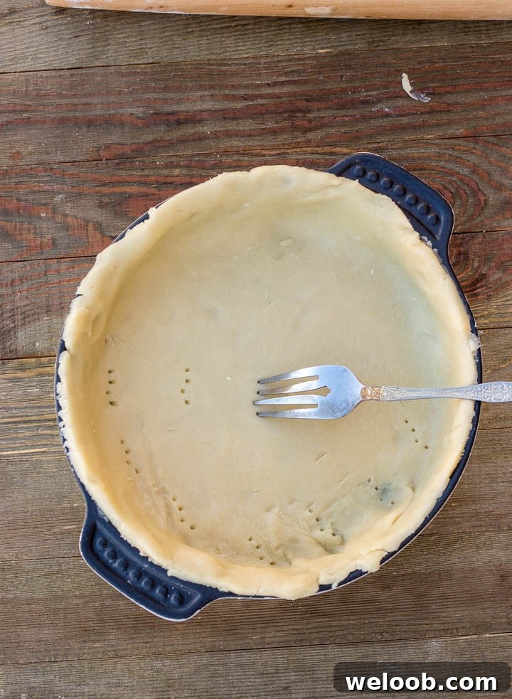 All butter crust in baking pan with a fork pricking the crust