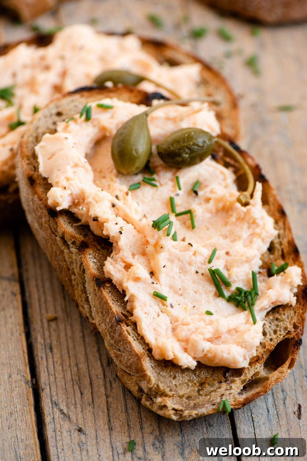 A close up of a slice of bread topped with smoked salmon pate, chives and capers.