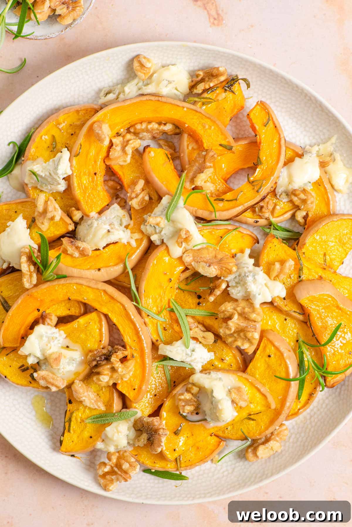 An overhead shot of roasted butternut squash on a serving plate with gorgonzola and walnuts