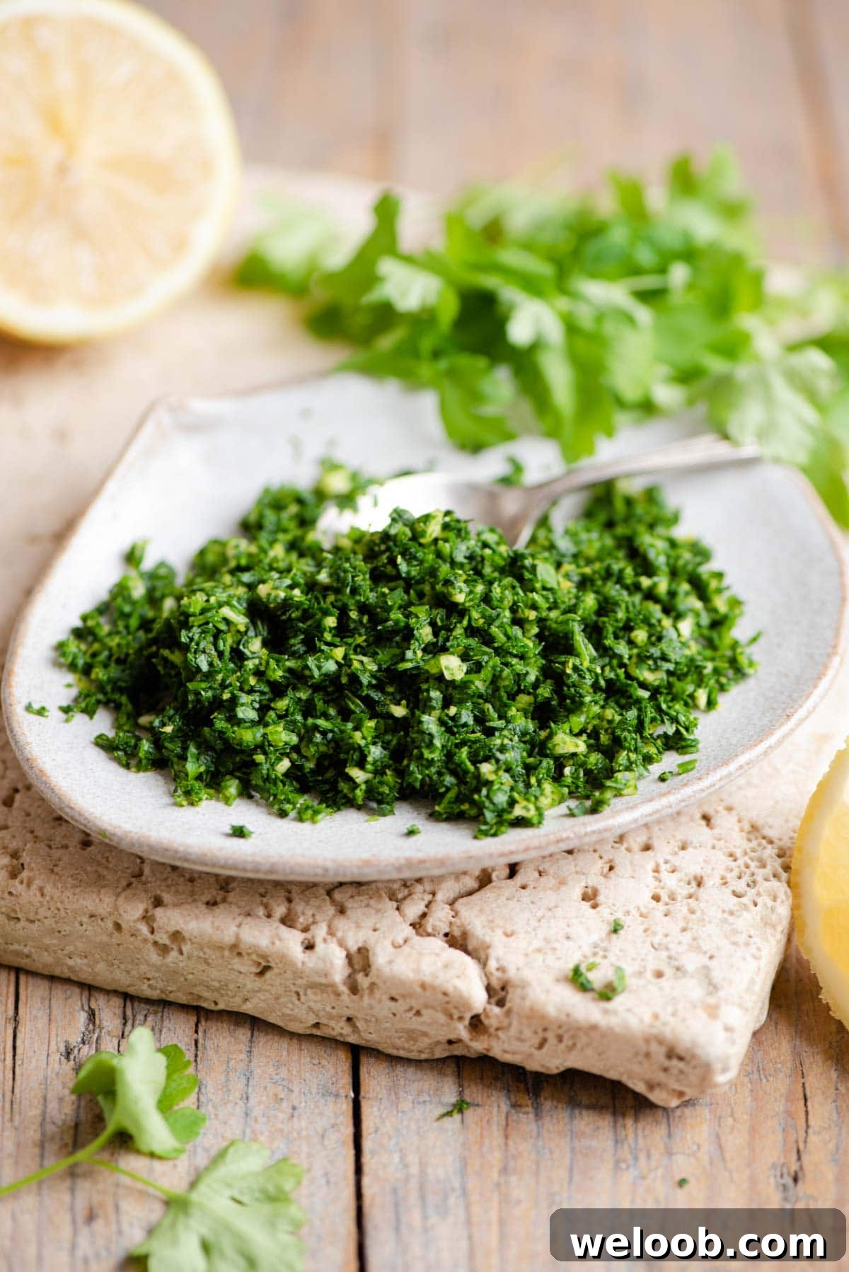Gremolata on a small plate with wedges of lemon and parsley in the background